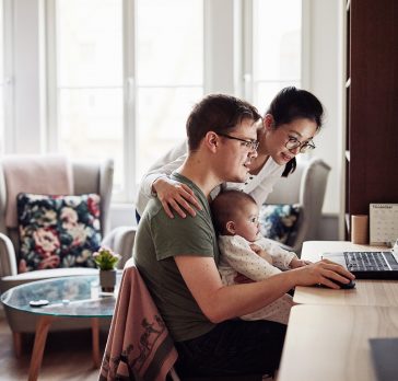 Shot of a couple looking at something on a laptop while sitting with their baby