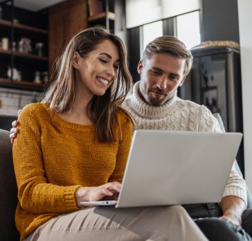 couple sitting on couch looking at laptop